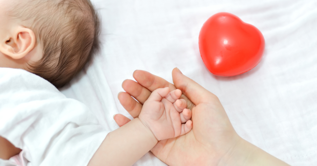 Mama drži bebinu ruku na dlanu, crveno srce pored
