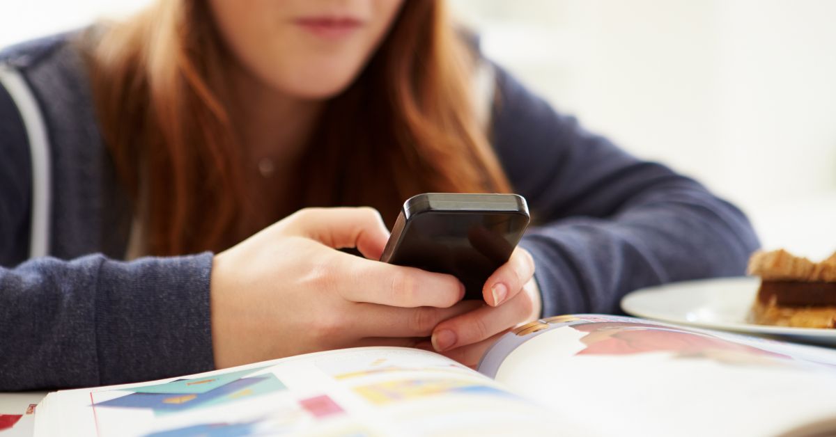 Devojčica drži mobilni telefon nad knjigom